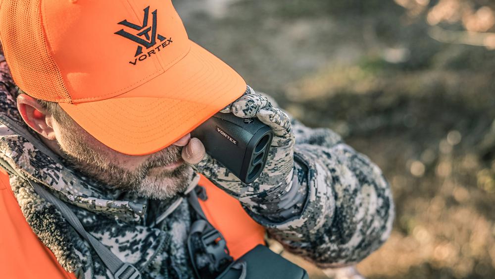 Midwestern hunter in a tree stand using a Vortex® rangefinder to glass for deer.