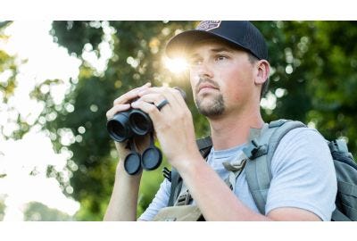 Mark Kenyon holding Vortex® binoculars on the edge of woods