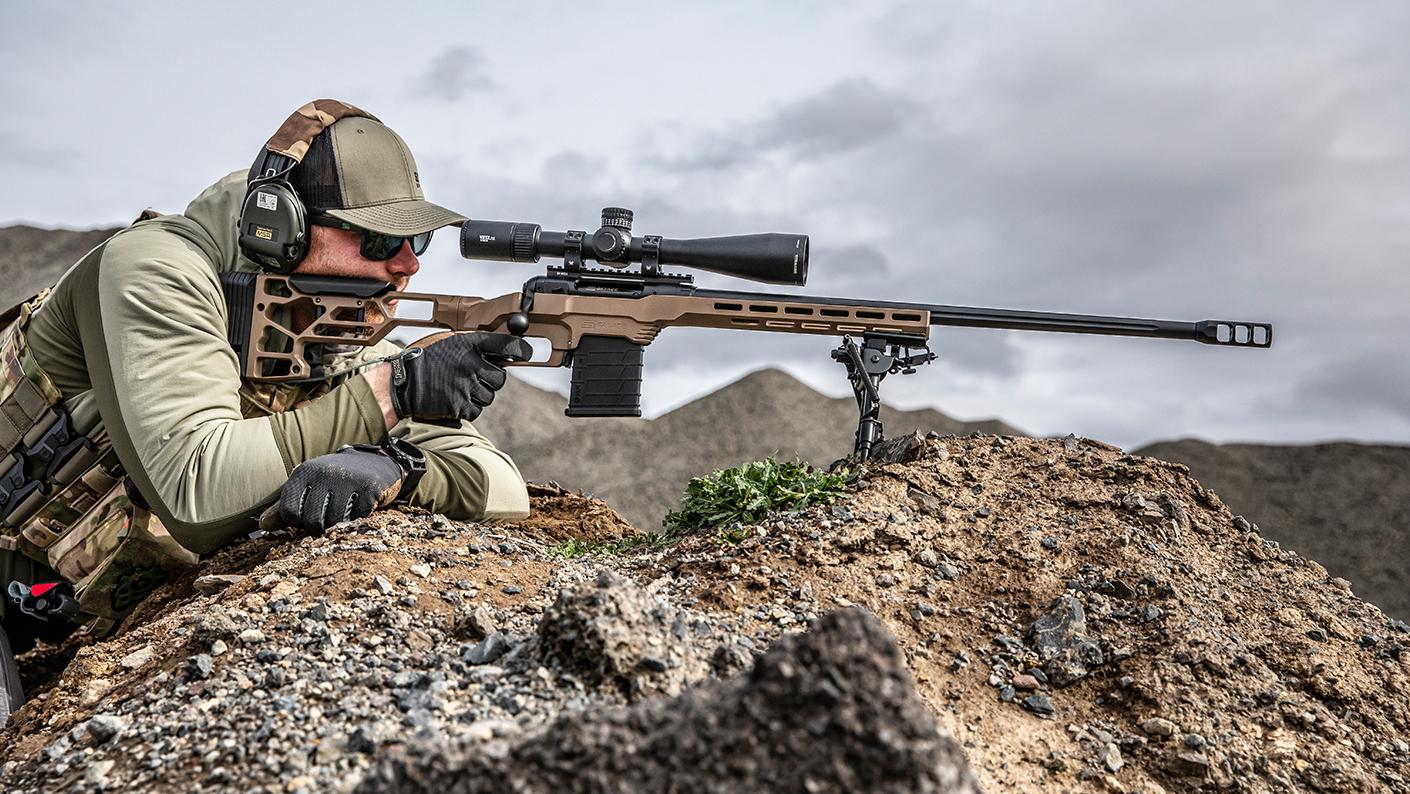 Shooter aiming rifle in rocky landscape.