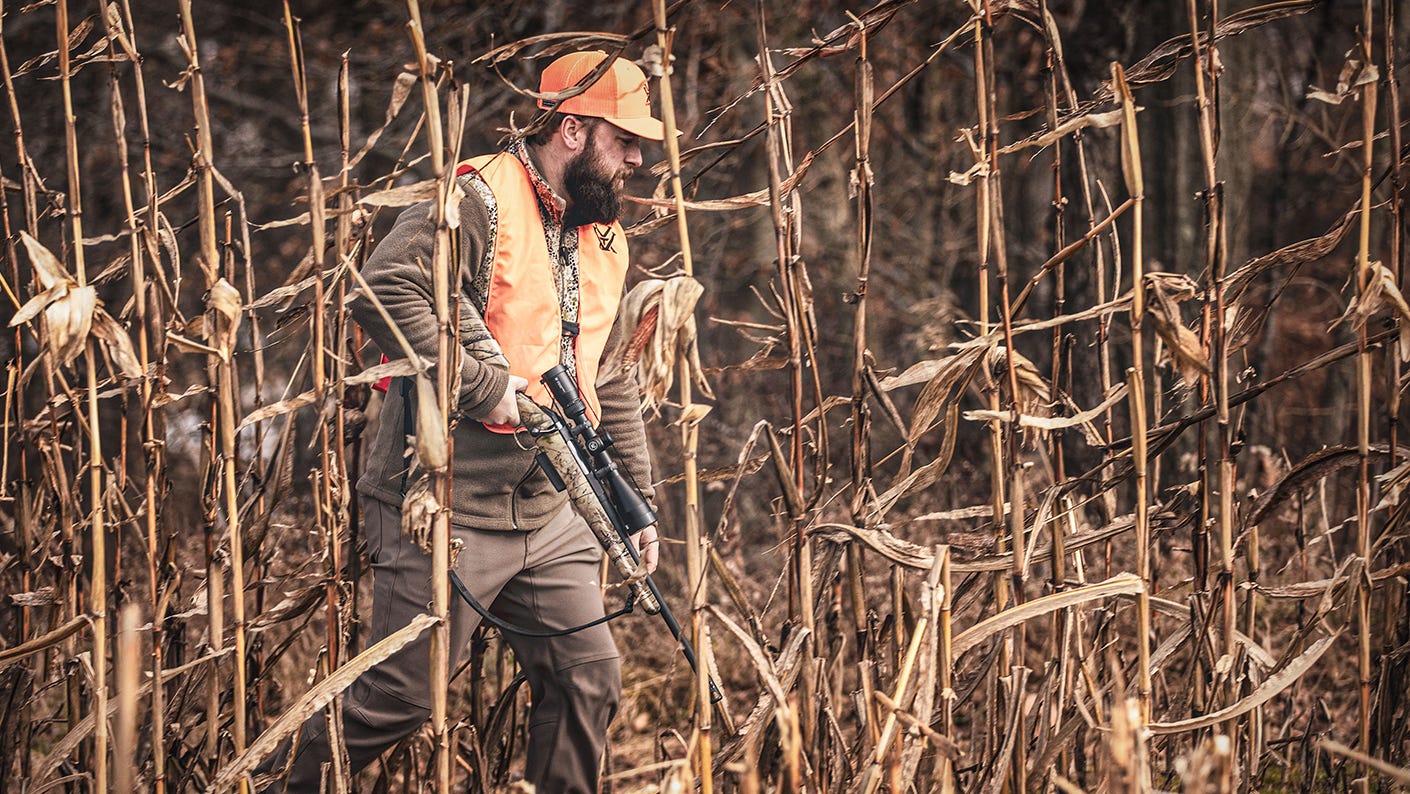 Mid-western hunter walking through a corn field with the Crossfire II Straight-Wall riflescope.